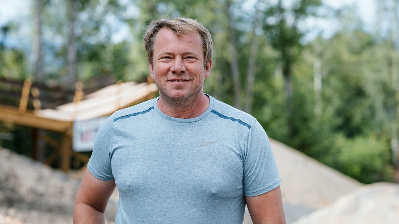 Mann med lys blå t-skjorte som står ute på en sykkepark og smiler til kameraet.