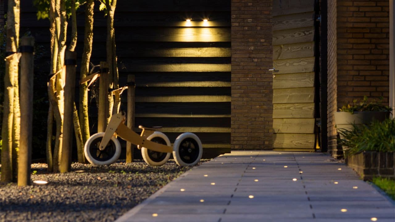 Opplyst gangsti til garasje og trehjulssykkel utenfor.