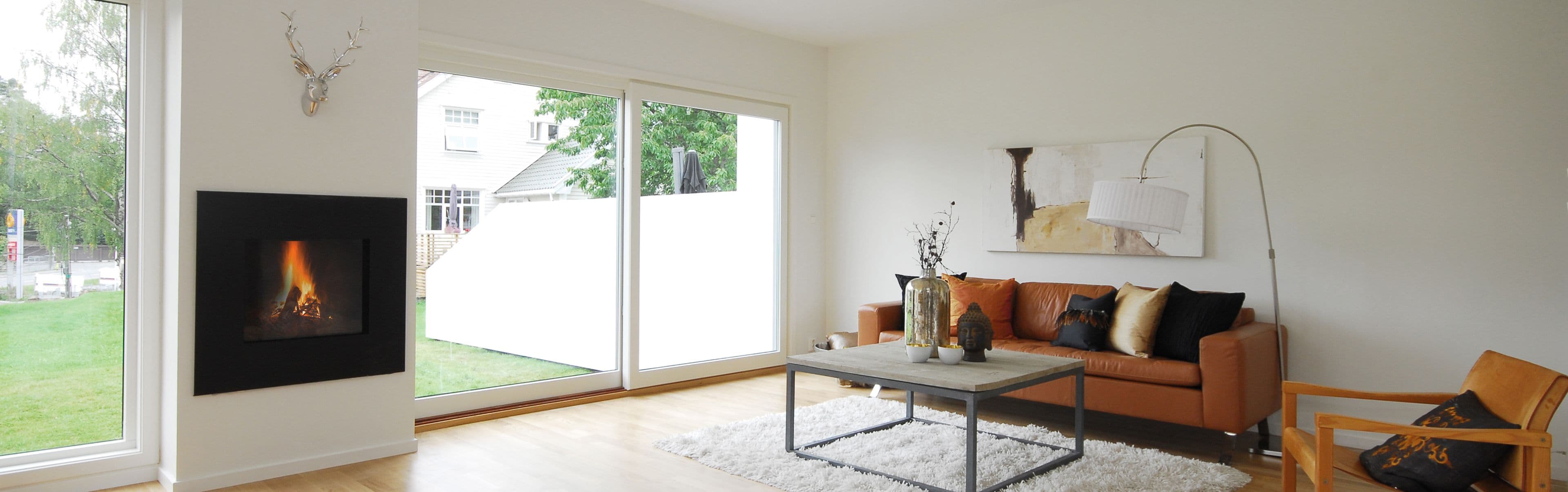 Moderne stue med store vinduer mot hagen og brun skinnsofa.