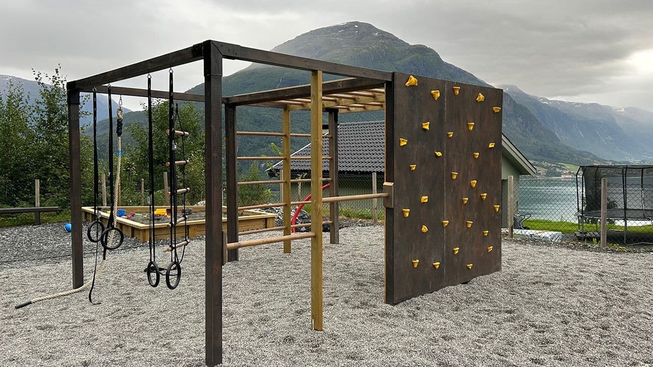 Lekestativ med klatrevegg og ringer på lekeplass ved havet.