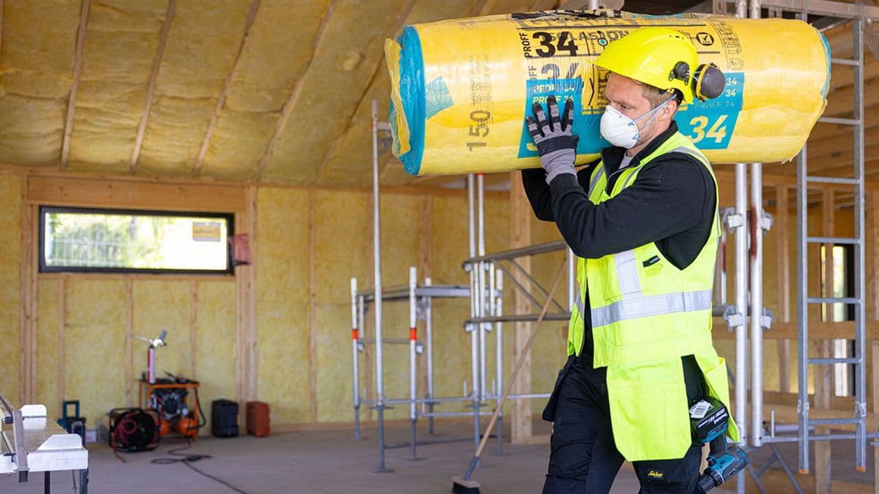Håndverker bærer en rull med Glava isolasjon over skulderen inne i et hus.