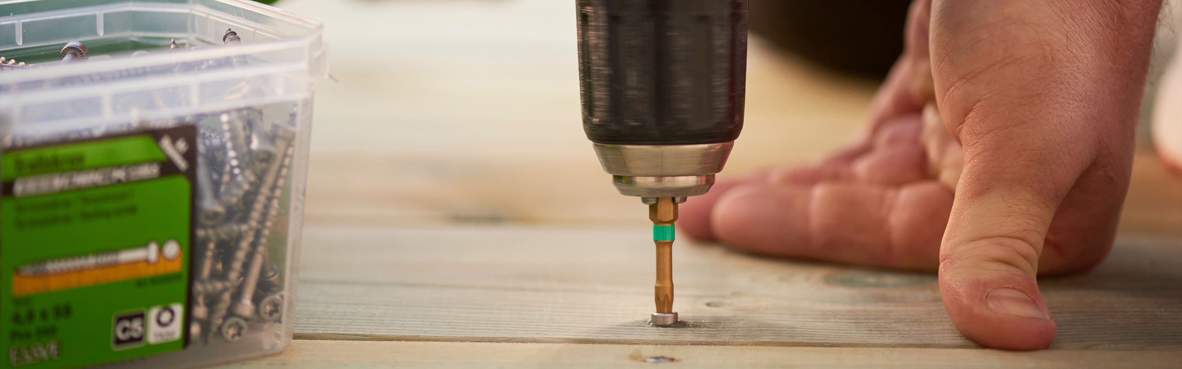 Nærbilde av drill som skrur inn syrefaste terrasseskruer i terrassebord.