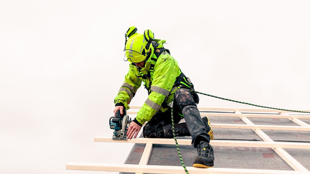Mann som arbeider på tak med sele og tau.