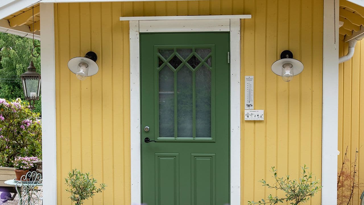Gult hus med klassisk ytterdør i grønn med glassfelt og sprosser.