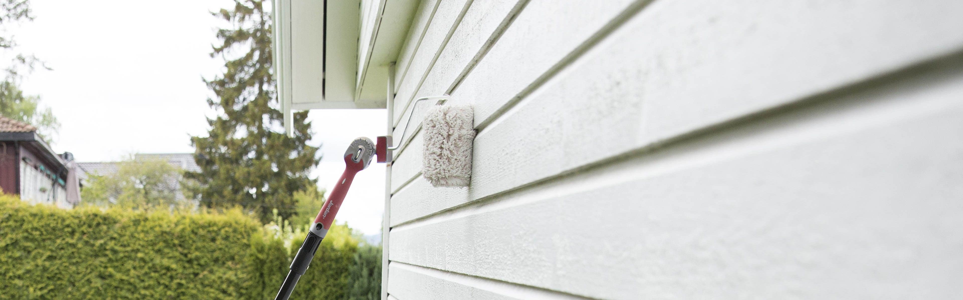 Nærbilde av male hus ute med malerulle og forlengerskaft.