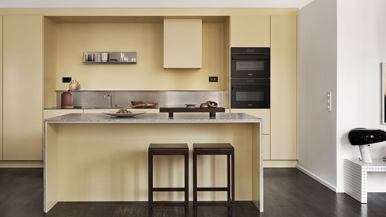 Lysegult kjøkken med benkeplate i stein og sorte hvitevarer.