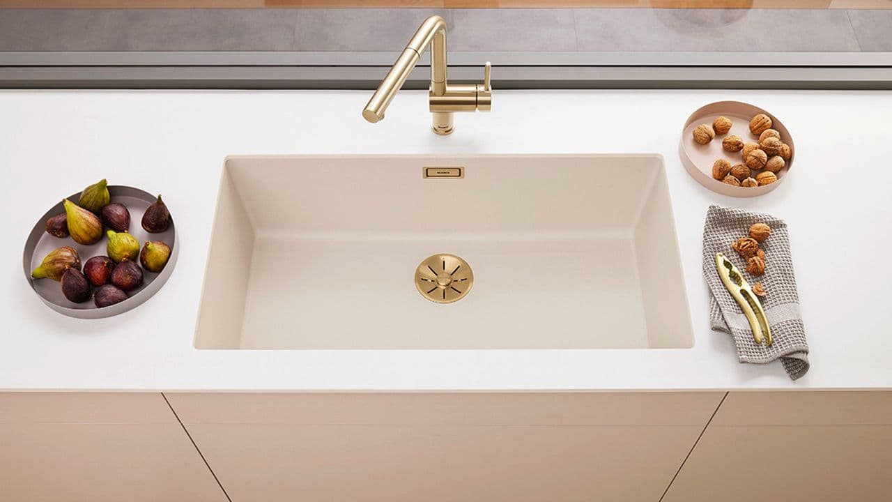 Nedfelt hvit kjøkkenvask i samme farge som benkeplaten og blandebatteri i messing.
