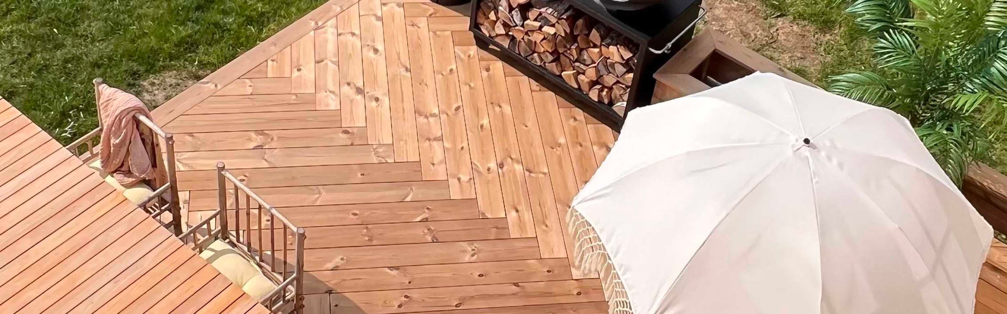 Terrasse i termofuru med fiskebeinsmønster med spisebord og parasoll sett i fugleperspektiv.