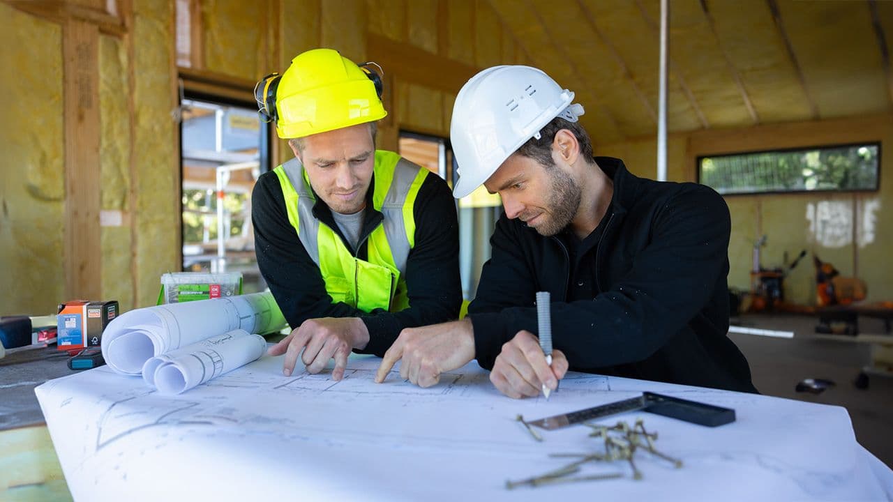 To menn som ser på plantegninger i et hus under bygging.