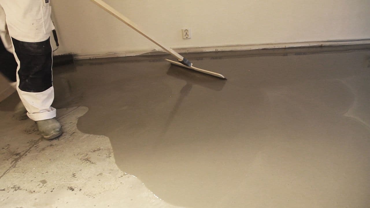 Mann som fordeler avrettingsmasse utover betonggulv.