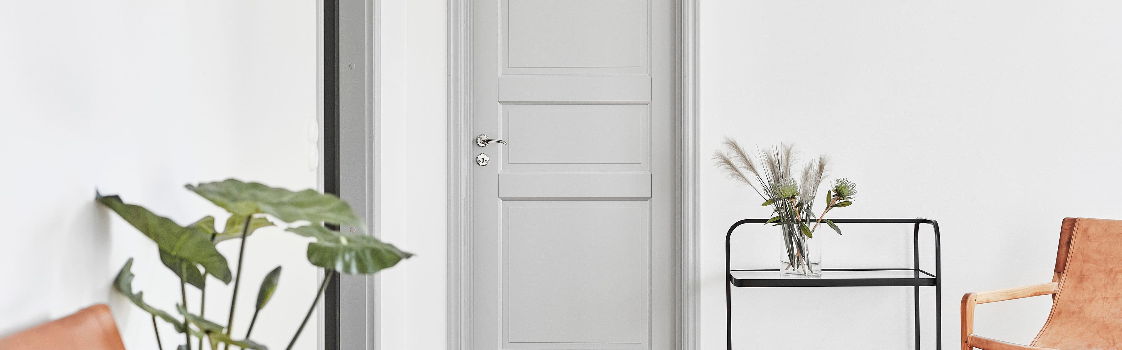 Lys grå innerdør med profil i stue med skinnstoler, grønne planter og trillebord.
