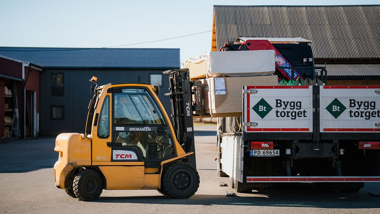 Truck som laster byggevarer på lastebil for å levere til byggeplass.