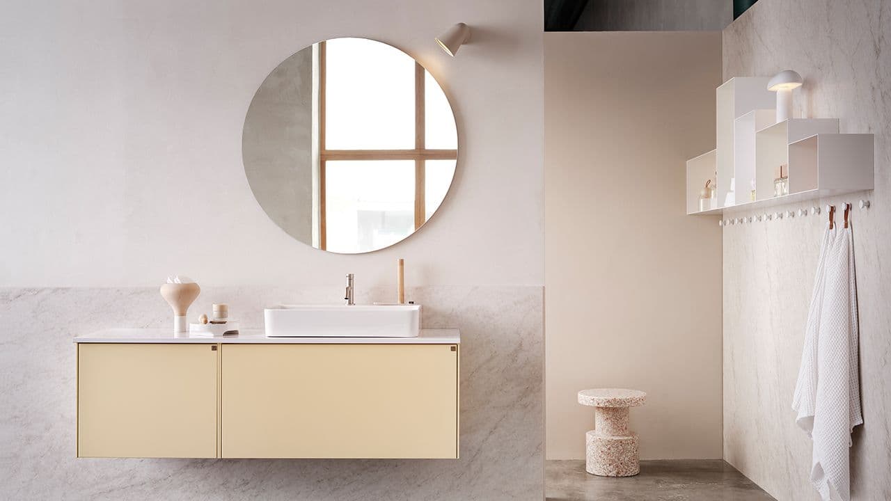 Bad med marmorvegger, gule baderomsmøbler og rundt speil.