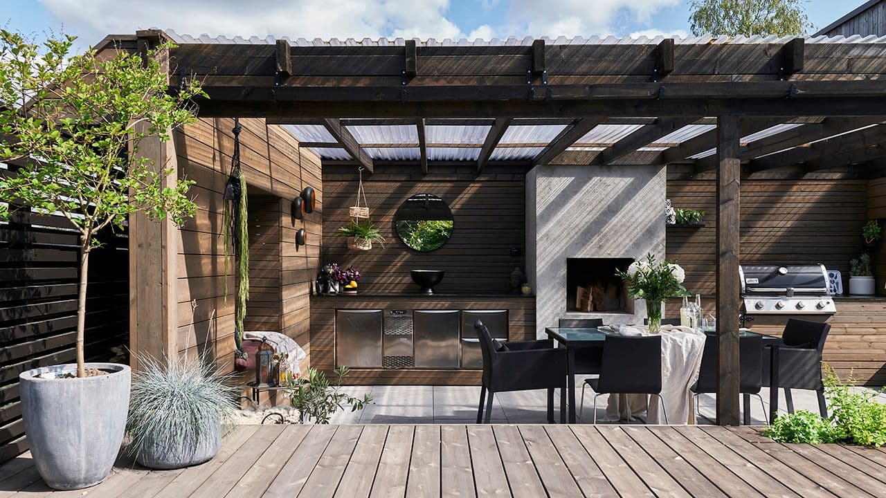 Uteplass med pergola med utekjøkken og spisebord.