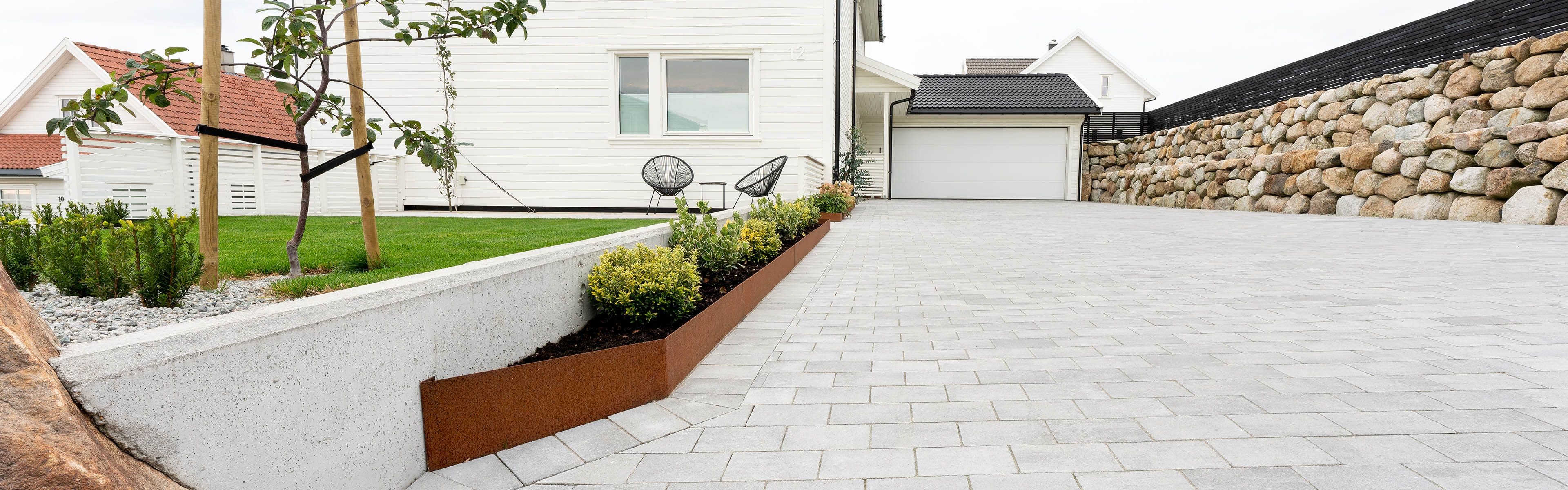 Multiblokk heller og mur i stein i oppkjørsel til hvitt hus.