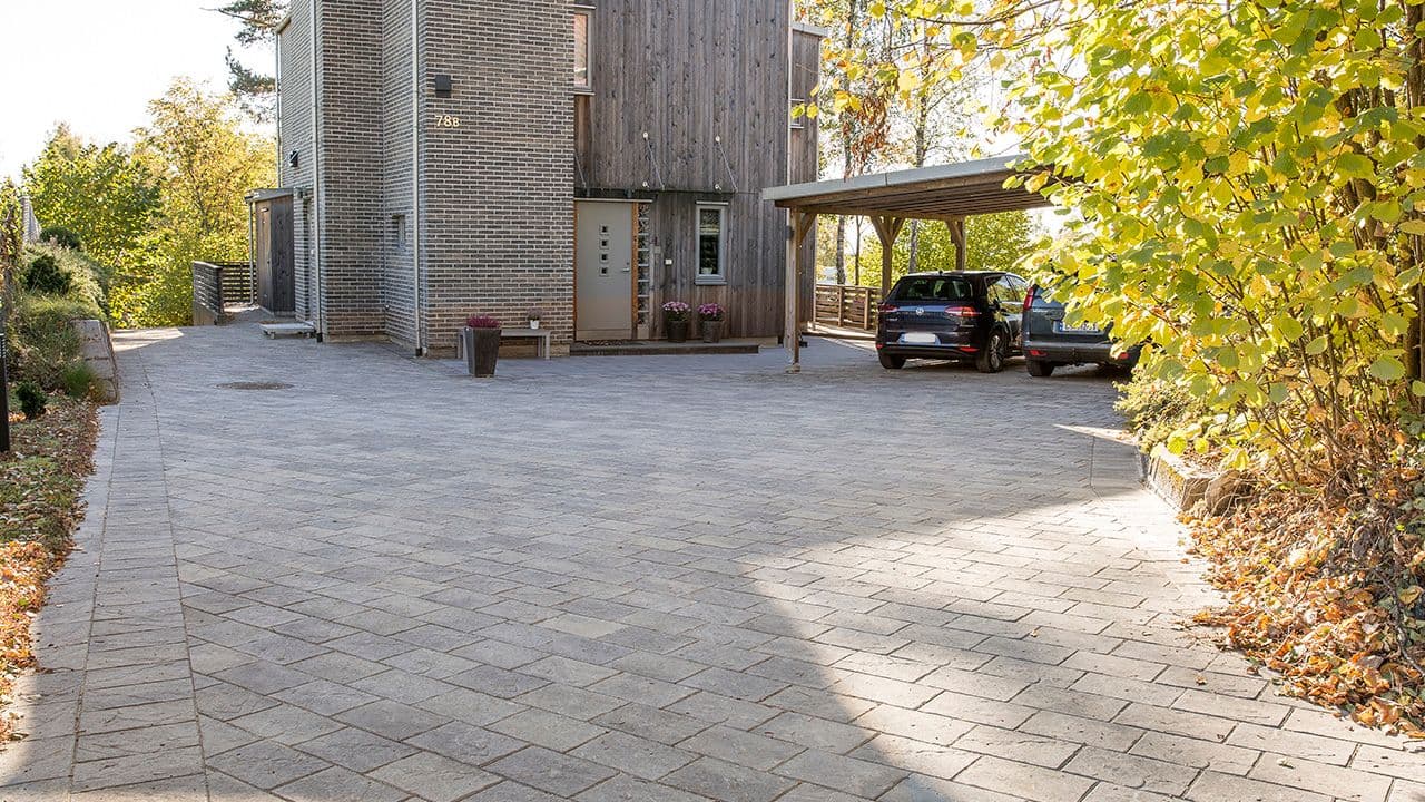 Funkishus i mur og tre med stor gårdsplass lagt med belegningsstein i halvforbandt mønster.