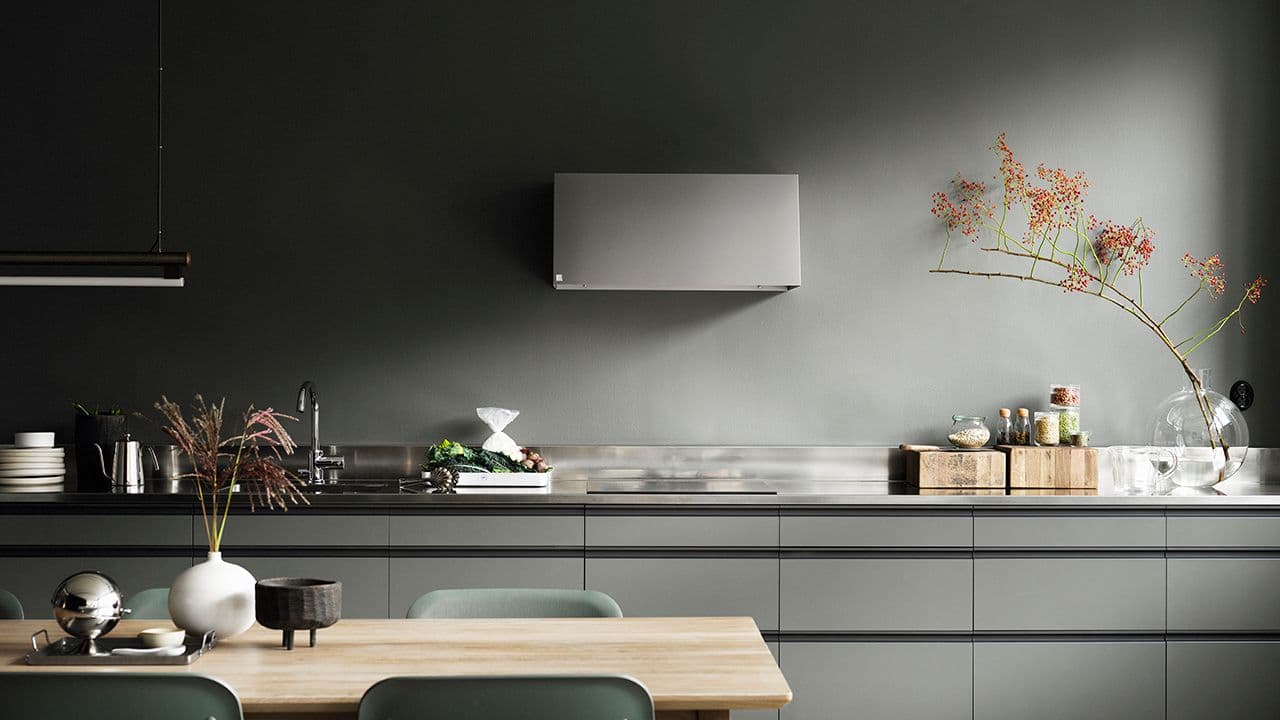 Grønt kjøkken med kjøkkenvifte og benkeplate i stål.