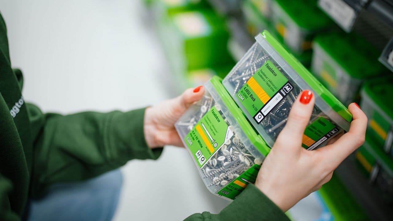 Hender som holder to bokser med fasadeskruer med skuehoder i svart og hvit.