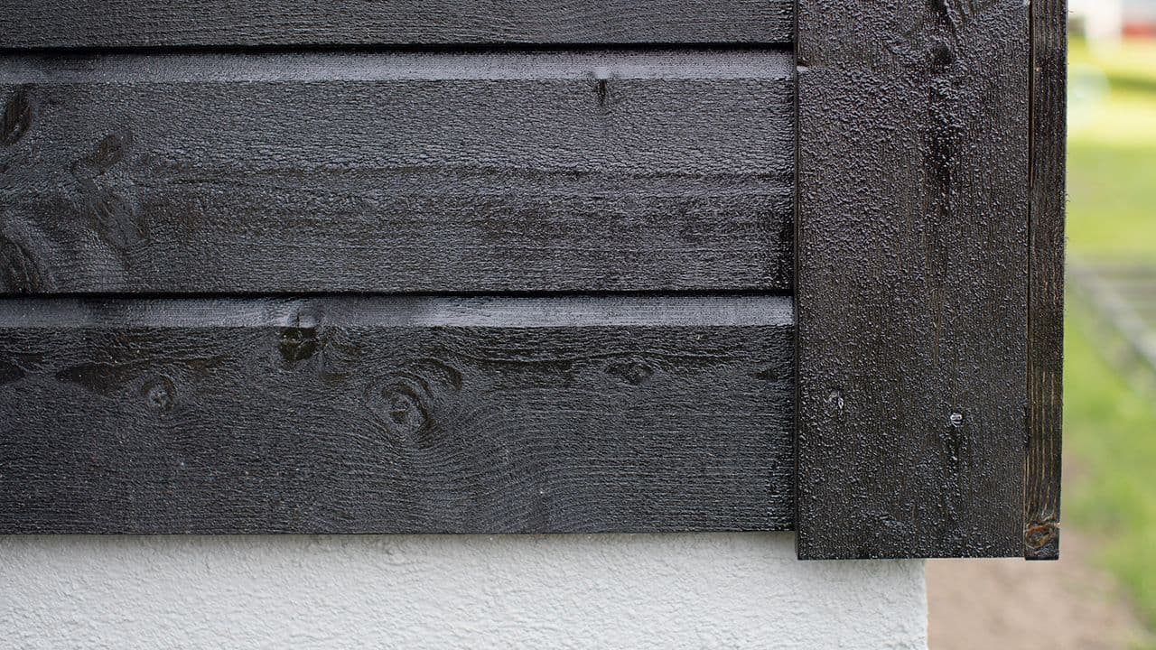 Nærbilde av sort dobbelfals kledning på hus med hvit grunnmur.