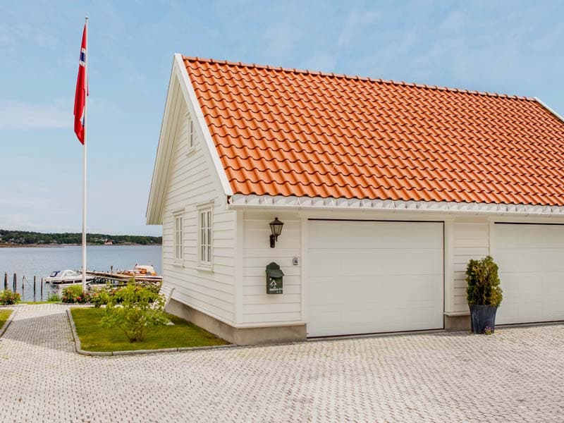 koselig hvitmalt garasje med rødt tak. flaggstang og sjøutsikt